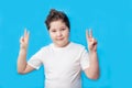 Little boy smiling joyfully and looking happy, feeling carefree and positive, holding both thumbs up on blue background