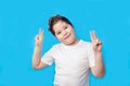 Little boy smiling joyfully and looking happy, feeling carefree and positive, holding both thumbs up on blue background