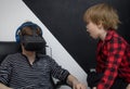 Little boy son is yelling at a young father who plays in a virtual reality glasses. Child needs attention from his father and Royalty Free Stock Photo