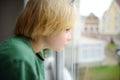 Little boy is standing in front of window, looking at the street, waiting for something. Lonely child at home. No friends, no Royalty Free Stock Photo
