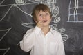 Little boy standing near the blackboard for drawing. Fingers holding in the mouth. Royalty Free Stock Photo