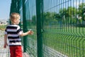 Little boy standing near grid fence