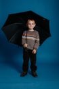 A little boy is standing under an open umbrella and smiling