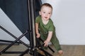 The little boy stands relying on the rack of the lighting unit.