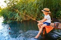 Little boy in straw hat sitting on the edge of a wooden dock and fishing in lake at sunset Royalty Free Stock Photo