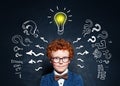 Little boy student in glasses with lightbulb on blackboard background. Brainstorming and idea concept Royalty Free Stock Photo