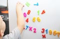 A little boy is studying the magnetic numbers on the fridge. Preschooler training