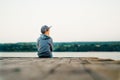 A little boy in a stylish cap and jacket looks out into the distance on the bridge near the lake. Royalty Free Stock Photo
