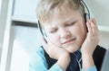 Cute 6 year old boy in suit listening to music or audio tutorial on headphones at the office background. Royalty Free Stock Photo