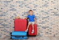Little boy with suitcases near brick wall