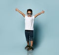 Little boy in sunglasses, white t-shirt, denim shorts, khaki sneakers. He is smiling, showing thumbs up, posing on blue background Royalty Free Stock Photo