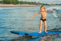 Little boy surfing on tropical beach. Child on surf board on ocean wave. Active water sports for kids. Kid swimming with