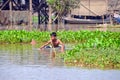 Little boy swimming in aluminum basin in the muddy water of the river Tonle Sap