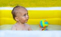 A little boy swims and plays with a colorful ball in an inflatable yellow pool. Royalty Free Stock Photo