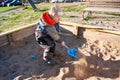 A little boy of three years old is playing on a cool spring sunny day in the sandbox in the city yard with his toy truck Royalty Free Stock Photo