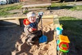 A little boy of three years old is playing on a cool spring sunny day in the sandbox in the city yard with his toy truck Royalty Free Stock Photo