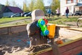 A little boy of three years old is playing on a cool spring sunny day in the sandbox in the city yard with his toy truck Royalty Free Stock Photo