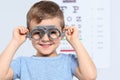Little boy with trial frame near eye chart in hospital, space for text Royalty Free Stock Photo