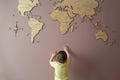 Little boy trying to get hold of a wooden world map on the wall Royalty Free Stock Photo