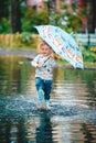 Little boy under colorful umbrella playing in summer park after rain