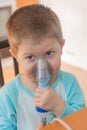 Little boy using nebulizer during inhaling therapy. Little boy making inhalation with nebulizer at home. Close up portrait of boy