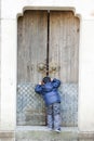 A little boy was lying in front of the wooden door and looked inside.