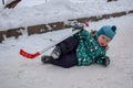 The little boy was tired of playing hockey and went to rest on the snow with a stick in winter in a park