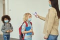 Little boy wearing face mask watching his teacher measuring temperature, screening kid with digital thermometer while Royalty Free Stock Photo