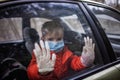 Little boy wearing respirator mask and medical gloves looking through a car window, stay safe Royalty Free Stock Photo