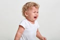 Little boy wearing t shirt cries, being in bad mood, looking away, posing isolated over white background, finding close person,