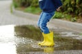 Little boy wearing yellow rubber boots jumping and having fun in puddle of water on rainy summer day in small town. Outdoors games Royalty Free Stock Photo