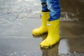 Little boy wearing yellow rubber boots jumping and having fun in puddle of water on rainy summer day in small town. Outdoors games Royalty Free Stock Photo