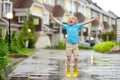 Little boy wearing yellow rubber boots jumping in puddle of water on rainy summer day in small town. Child having fun Royalty Free Stock Photo