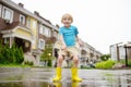 Little boy wearing yellow rubber boots jumping in puddle of water on rainy summer day in small town. Child having fun Royalty Free Stock Photo