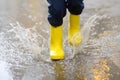 Little boy wearing yellow rubber boots jumping in puddle of water on rainy summer day in small town. Child having fun Royalty Free Stock Photo