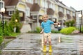 Little boy wearing yellow rubber boots jumping in puddle of water on rainy summer day in small town. Child having fun Royalty Free Stock Photo