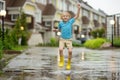 Little boy wearing yellow rubber boots jumping in puddle of water on rainy summer day in small town. Child having fun Royalty Free Stock Photo