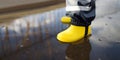 Little boy wearing yellow rubber boots jumping in puddle of water on rainy summer day in small town. Child having fun. Outdoors Royalty Free Stock Photo