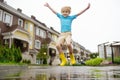 Little boy wearing yellow rubber boots jumping in puddle of water on rainy summer day in small town. Child having fun Royalty Free Stock Photo