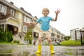 Little boy wearing yellow rubber boots jumping in puddle of water on rainy summer day in small town. Child having fun. Outdoors Royalty Free Stock Photo