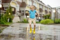 Little boy wearing yellow rubber boots jumping in puddle of water on rainy summer day in small town. Child having fun. Outdoors Royalty Free Stock Photo