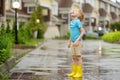 Little boy wearing yellow rubber boots walking on rainy summer day in small town. Child having fun. Kid catches raindrops with Royalty Free Stock Photo