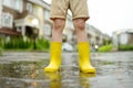 Little boy wearing yellow rubber boots walking on rainy summer day in small town. Child having fun. Games for children in rain