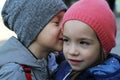 Little boy whispers a secret to girl wearing winter hats
