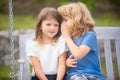 Little boy whispers to lovely girl in ear. Brother and sister playing in spring park outdoors. Little boy and girl kids