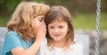 Little boy whispers to lovely girl in ear. Two children outdoors. Portrait of adorable brother and sister smile and Royalty Free Stock Photo