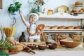 little boy in white chef uniform holding a loaf and candy in the bakery, bread shop Royalty Free Stock Photo