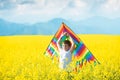 Little boy in white shirt running with kite in the booming yellow field