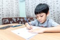 Little boy writing homework on wooden table at home. Kid learing and writing alphabet looking very happy