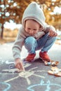 Little boy 3-6 years old, in autumn on street, draws on pavement, colorful crayons. Warm clothes on a cold day, beige